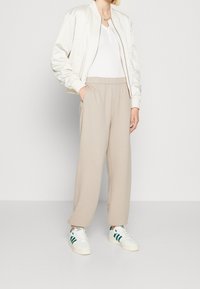 Bílá bomber bunda s žebrovanými manžetami, béžové tepláky s elastickým pasem a bílé tenisky se zelenými pruhy. Jednoduchý a pohodlný střih.