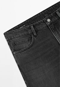 Gros plan sur un jean en denim noir montrant la poche avant, les passants de ceinture, la fermeture à bouton, et l'étiquette de la marque Massimo Dutti à l'intérieur de la ceinture.