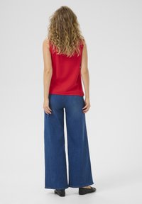 Top rojo sin mangas combinado con pantalones vaqueros anchos de mezclilla azul. El conjunto presenta una textura suave, un ajuste casual y un diseño de color sólido.