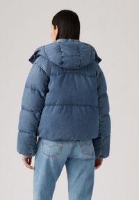 Denim pufferjack met capuchon, met een gewatteerd ontwerp in een middelblauwe kleur. Zachte textuur en een losse pasvorm met verlaagde schouders.