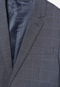 Blazer grigio con un motivo a quadri che presenta linee blu. Il tessuto ha una trama sottile, e l'interno è foderato con un materiale liscia di colore blu navy.