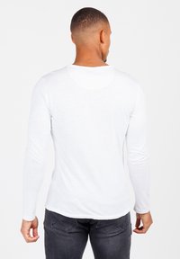 Wit T-shirt met lange mouwen, ronde halslijn, gladde textuur en een aansluitende pasvorm, gedragen met donkere spijkerbroek, gezien van de achterkant.