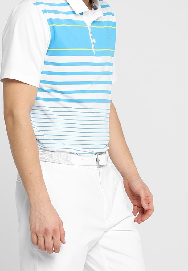 Homme portant un polo rayé bleu et blanc, avec un pantalon blanc et une ceinture blanche, debout devant un fond uni.