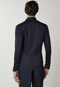 Camicia a maniche lunghe blu marina con una forma aderente, texture liscia e dettagli con bottoni sui polsini; design minimalista, senza motivi visibili.