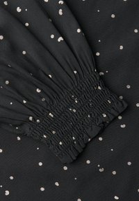 Musta kangas, jossa on metallinhohtoisia kultaisia pilkkuja, varustettuna kerroksittaisella joustinvarttisomisteella. Sileä pinta ja kevyt muotoilu.