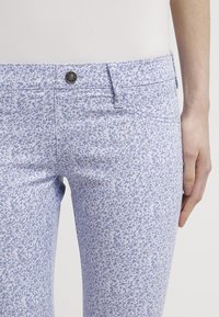 Pantalones con estampado floral en azul claro y blanco, hechos de tejido suave. Tienen una cintura estándar con un botón metálico y bolsillos delanteros.