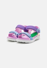 Sandalias coloridas con una parte superior de tela en tonos rosa y púrpura, correas ajustables, plantilla acolchada y suela de goma blanca.