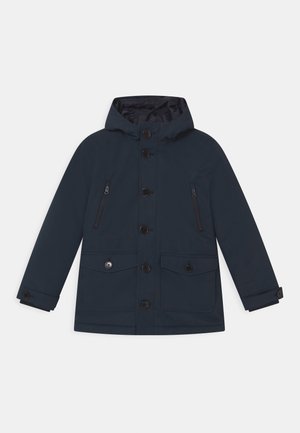 Manteau à capuche bleu foncé avec boutons à l'avant, deux poches poitrine zippées et deux poches à rabat boutonné à la taille, présenté sur un fond uni.
