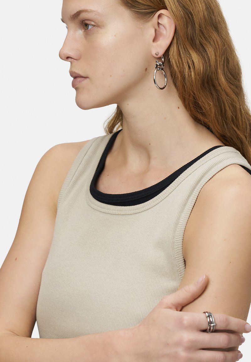 Beige ribbad linne med en svart kontrasterande halsringning. Bärs med silverfärgade hoop-örhängen och flera silverringar, med en avslappnad passform.