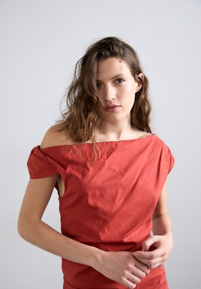 Top roșu off-the-shoulder, realizat dintr-un material ușor, cu mâneci scurte, croială lejeră și textură netedă.