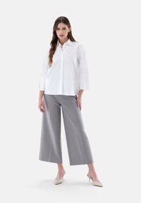 Weiße Bluse mit drei Viertelärmeln, kombiniert mit grauen weiten Hosen. Beigefarbene Absätze runden das Outfit ab. Glatte Stofftextur.
