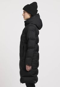 Zwarte pufferjas met een capuchon, featuring een quilted ontwerp, lange mouwen, zijzakken en een knielange snit. Draagt een bijpassende beanie.