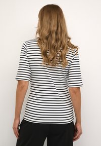 Tricou rayé alb-negru cu mâneci scurte și decolteu rotund, realizat dintr-un material moale, purtat cu pantaloni negri.