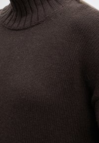 Gros plan d’un pull à col roulé tricoté marron foncé montrant le col côtelé et le tissu texturé.