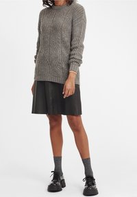 Szary sweter robiony na drutach z żeberkową teksturą i okrągłym dekoltem, zestawiony z czarną skórzaną spódnicą. Modelka ma na sobie szare skarpetki w wzory i masywne czarne buty.