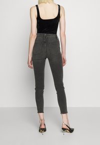Svart sammetslinne utan ärmar som kombineras med grå högmidjade skinny jeans, med fem fickor och fransad nederkant, accessoriserad med svarta klackar.