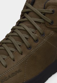 Κοντινό πλάνο καφέ δερμάτινου μποτάκου πεζοπορίας με δαντέλες ελιάς και μαύρα οπές, που δείχνει λεπτομερή ραφή και μέρος της μαύρης σόλας.