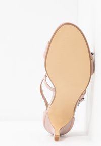 Rosa High-Heel Sandale mit glattem, glänzendem Obermaterial, verstellbarem Riemen und strukturiertem beigem Fußbett. Runde Zehenpartie und minimale Details.