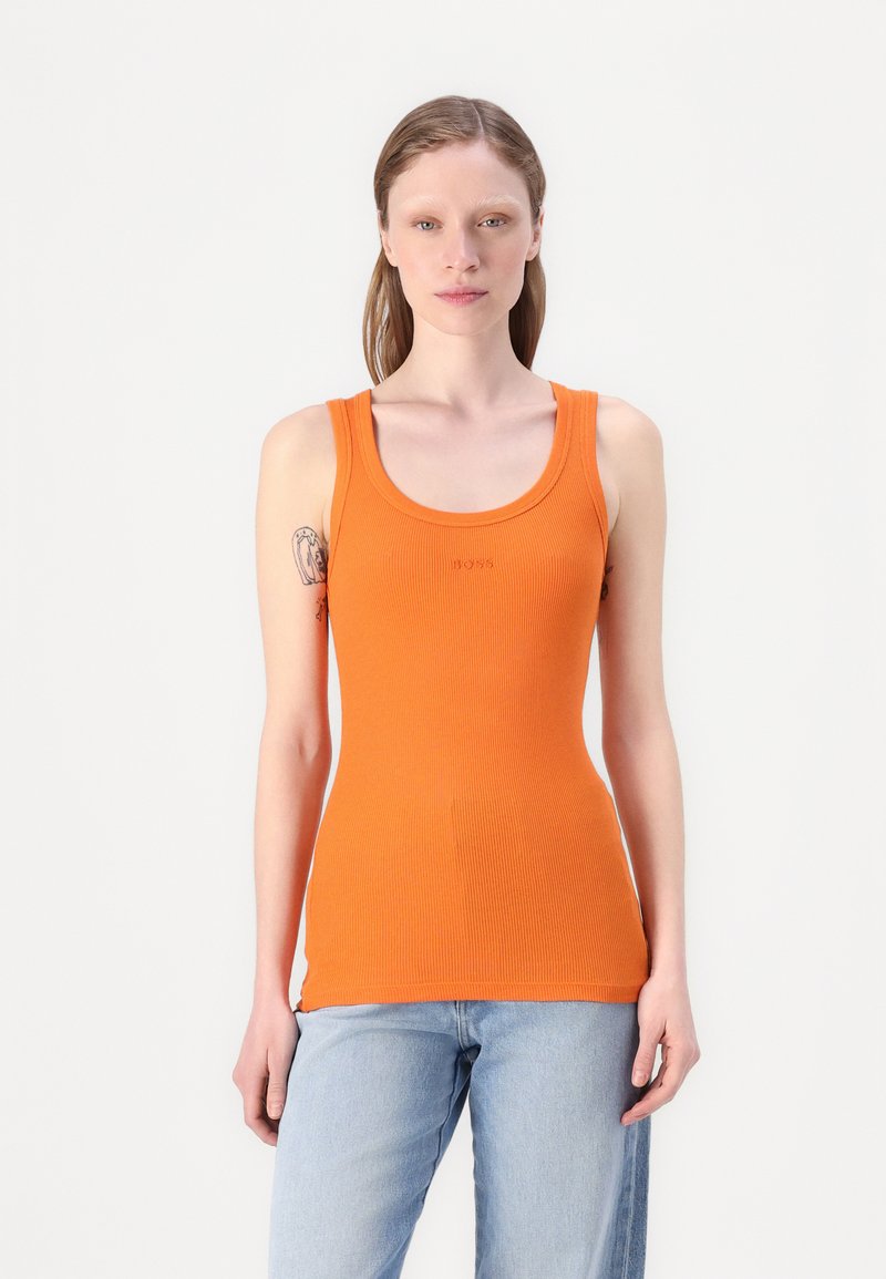 Top de tirantes naranja con canalé, escote redondeado y tirantes anchos, combinado con jeans rectos de lavado claro. Detalle sutil de la marca en el pecho.