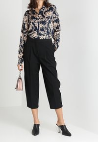 Námořnická květinová košile s dlouhým rukávem a světle růžovým vzorem, kombinována s černými kalhotami širokého střihu. Černé muly s bílými blokovými podpatky. Světlá kabelka.