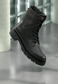 Czarne skórzane botki za kostkę z zapięciem na sznurówki, okrągłym noskiem i masywną gumową podeszwą. Posiada złote akcenty na obcasie.