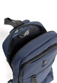 Námorně modrý batoh vyrobený z texturovaného nylonu, s přední kapsou, zipovým uzávěrem a vnitřním panelem s designem značky. Součástí jsou nastavitelné popruhy.
