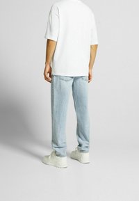 Camiseta blanca de gran tamaño, jeans de mezclilla azul claro y zapatillas blancas. Ajuste casual con una forma relajada y detalles de costuras visibles.
