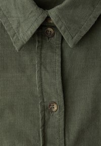 Gros plan sur le col d'une chemise en velours côtelé vert olive et la patte de boutonnage avec deux boutons marron et des détails de coutures visibles.