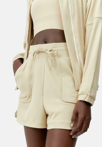 Pantalones cortos deportivos beige hechos de una tela suave, con bolsillos laterales, cintura con cordón y una textura suave.