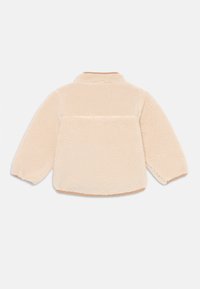 Beige, langärmlige Fleecejacke mit hohem Kragen, von hinten betrachtet, mit einer weichen, strukturierten Oberfläche und leicht geschwungenem Saum.