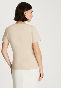 Beżowa koszulka z krótkim rękawem o okrągłym dekolcie, miękka w dotyku, dopasowana, z subtelnymi szwami, w zestawie z białą dżinsową spódnicą.