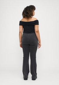 Svart off-shoulder topp med plisserad detalj, i kombination med mörkgrå utsvängda jeans med sömnadsdetaljer och en slät textur.