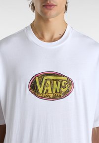 Witte katoenen t-shirt met een groot, kleurrijk Vans-logo in een bruine ovaal met roze accenten, ronde halslijn en korte mouwen.