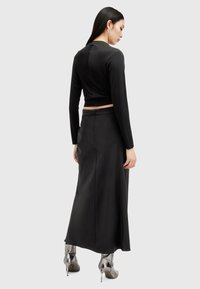 Zwarte crop top met lange mouwen, gecombineerd met een zwarte satijnen maxi rok. De rok heeft een slit aan de achterkant en een verborgen rits. Metallic hakken.