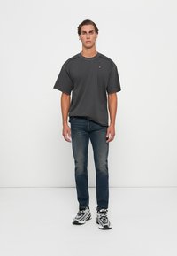 Grå kortermet t-skjorte med rund hals og udekorerte detaljer, sammen med mørkeblå tettsittende jeans og svarte sneakers med hvite detaljer.