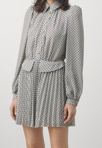 Vestito con motivo a fantasia bianco e nero, maniche lunghe, scollo con colletto, bottoni dorati, vita aderente e gonna plissettata.