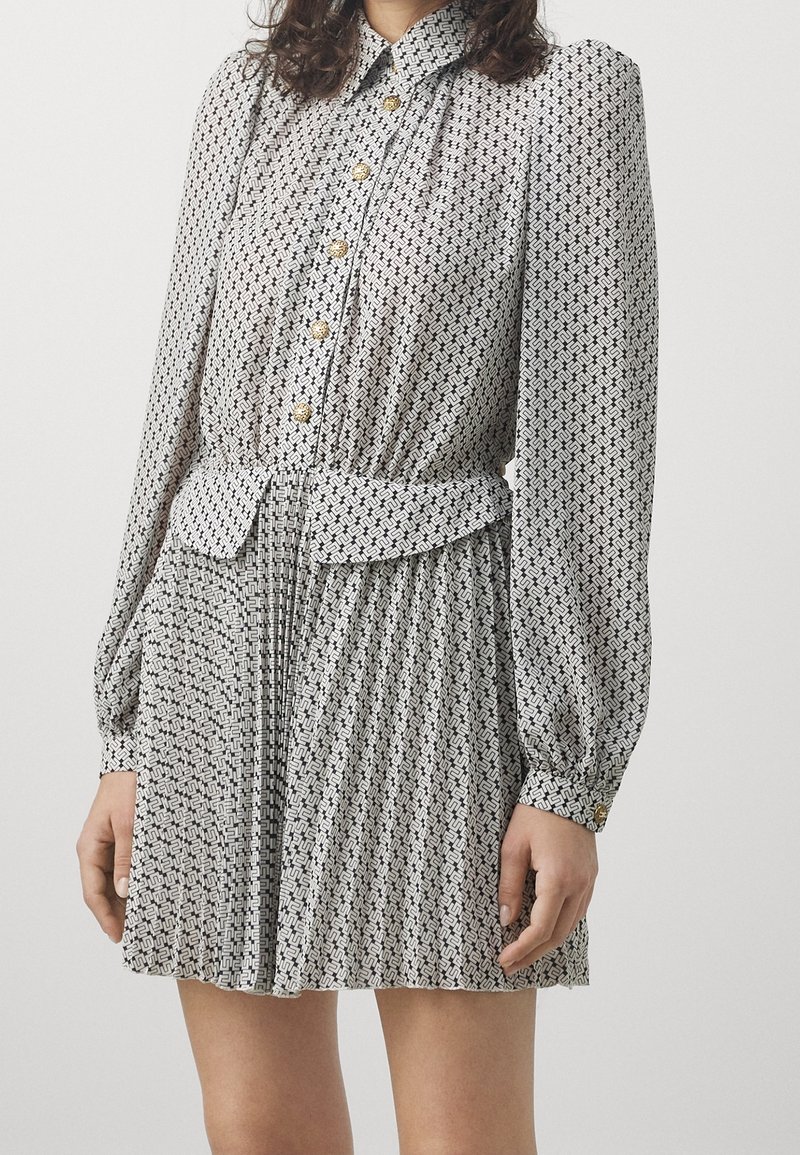 Vestito con motivo a fantasia bianco e nero, maniche lunghe, scollo con colletto, bottoni dorati, vita aderente e gonna plissettata.