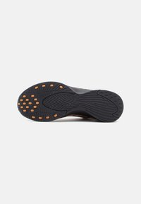 Svart sneakersåle med oransje grep-dots, intrikat dekkmønster og buet design for forbedret grep og fleksibilitet.