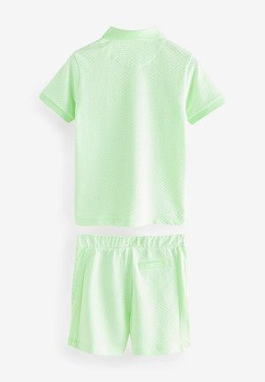 Gaiši zaļš īss piedurkņu polo krekls ar smalku rakstu, apvienots ar atbilstošām šortiem ar elastīgu jostu un sānu kabatu.
