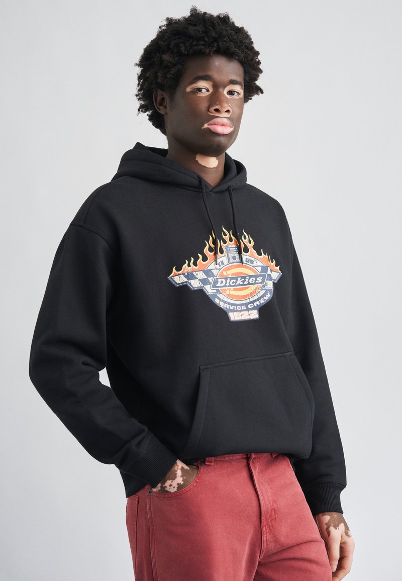 Black hoodie with graphic design featuring flames and a circular logo. Material appears soft; features a front pocket and adjustable drawstring.