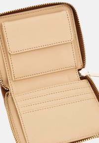 Tan leather wallet interior with multiple card slots, a flap pocket, and gold-tone zipper detail along the edge. Smooth texture throughout.