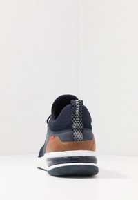 Navy sneaker with mesh upper, brown leather accents, white sole, and patterned heel tab. Features contrasting red detail near the heel.
