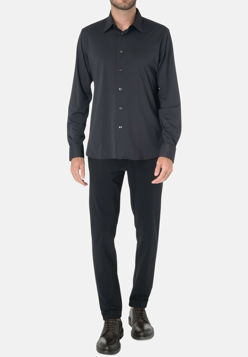 Camicia nera a maniche lunghe con bottoni, realizzata in tessuto liscio, con colletto classico e chiusura frontale a bottoni. Indossata con pantaloni neri a gamba dritta.