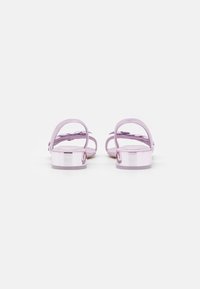 Sandales lilas avec un talon rose brillant, présentant de fines lanières et un accent en nœud. La semelle est plate et texturée pour une meilleure adhérence.