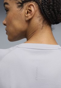 A világos szürke sportpóló texturált anyagot mutat be bordázott nyakkivágással. Finom varrási részlet látható a felső háton.