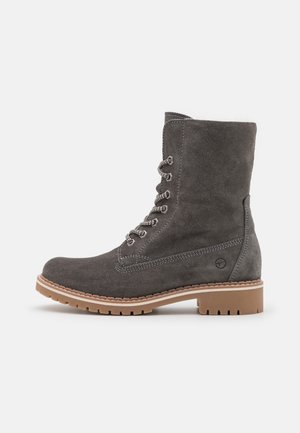 Bottine à lacets en daim gris foncé avec semelle en caoutchouc beige et petit talon, détail logo sur le côté et semelle crantée robuste pour une utilisation extérieure.