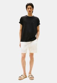 T-shirt nera a maniche corte con risvolti, pantaloni corti bianchi e sandali beige con cinturino. Design semplice, materiale in cotone, vestibilità casual.