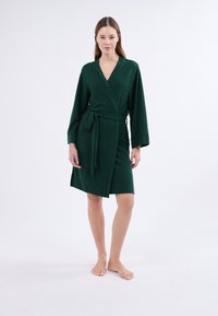 Tmavě zelený plášť s oboustranným designem, širokými rukávy, zavazováním v pase a délkou ke kolenům. Měkká textura, minimalistický styl.