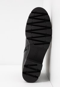 Semelle de chaussure noire avec un motif de traction géométrique, présentant une texture lisse et un logo. Fabriquée en matériau en caoutchouc durable.