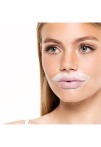 Ung kvinne med klare blå øyne og lange øyevipper som bruker en gjennomsiktig leppemaske på leppene mot en hvit bakgrunn.